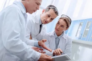 scientists in laboratory discussing research data on tablet wearing lab coats and safety goggles