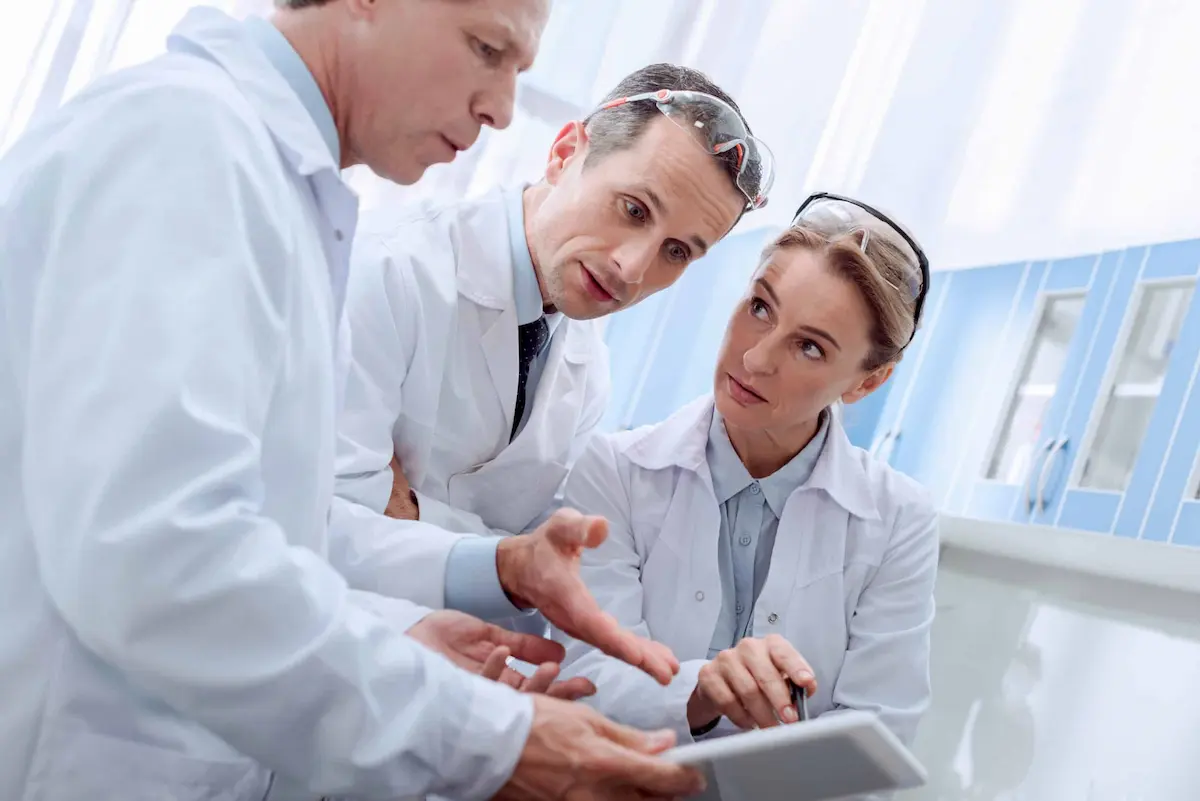 scientists in laboratory discussing research data on tablet wearing lab coats and safety goggles