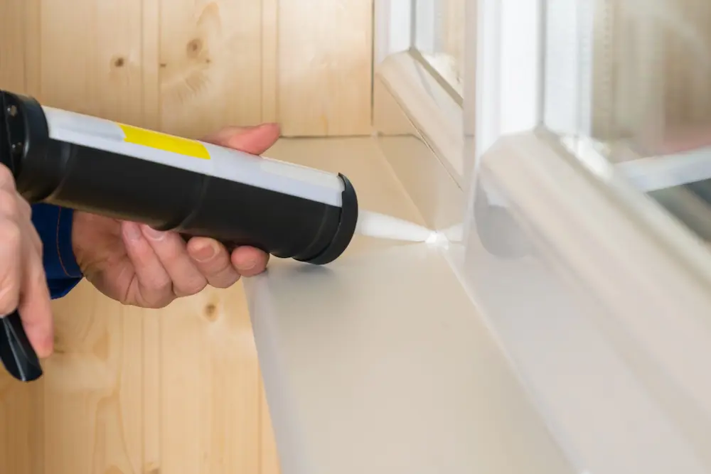 A man applying caulk and sealant around windows and gaps in a house to prevent pests from entering.